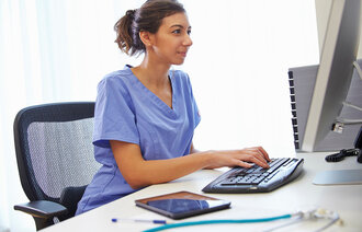Bildet viser en kvinnelig sykepleier som skriver på et tastatur