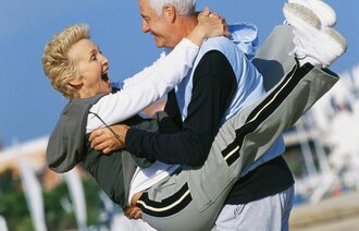 Bilde av eldre kvinne som hopper opp på en eldre mann. Begge smiler og ler