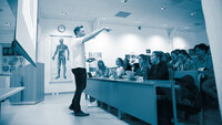 The photo shows a male lecturer in an auditorium full of female students