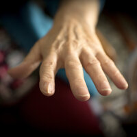 Bildet viser en eldre kvinnes hånd som strekker seg ut etter noe eller noen