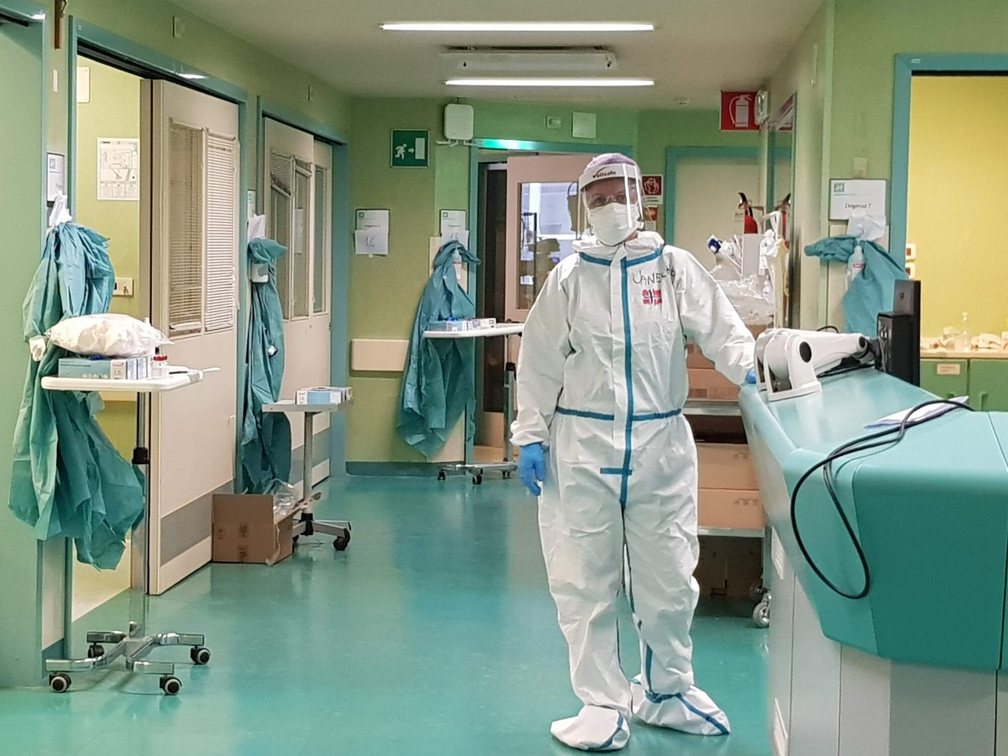Bildet viser en sykepleier i smittevernutstyr i en sykehuskorridor.