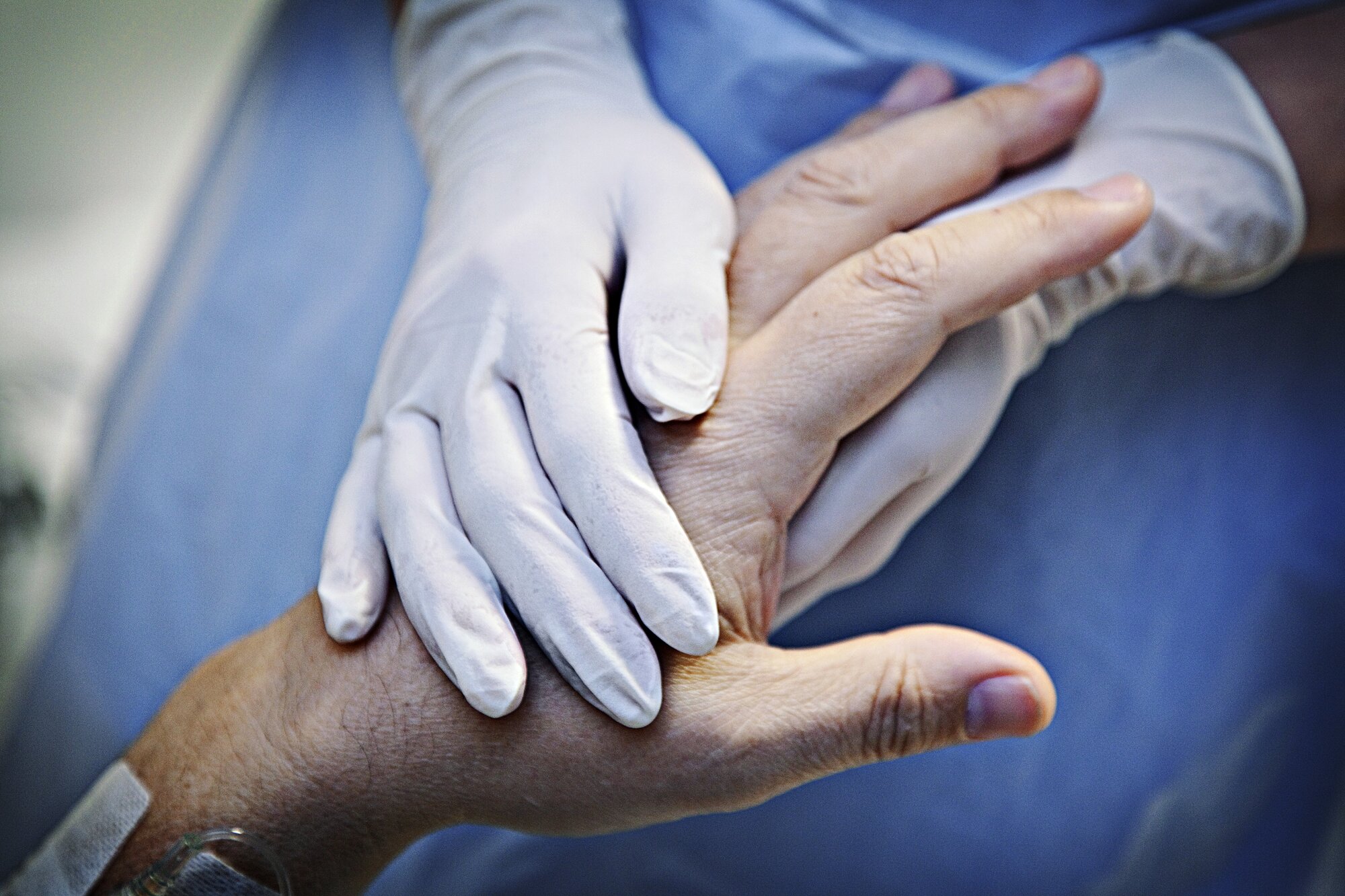 Bildet viser et par hender med plasthansker som holder hånda til en gammel person