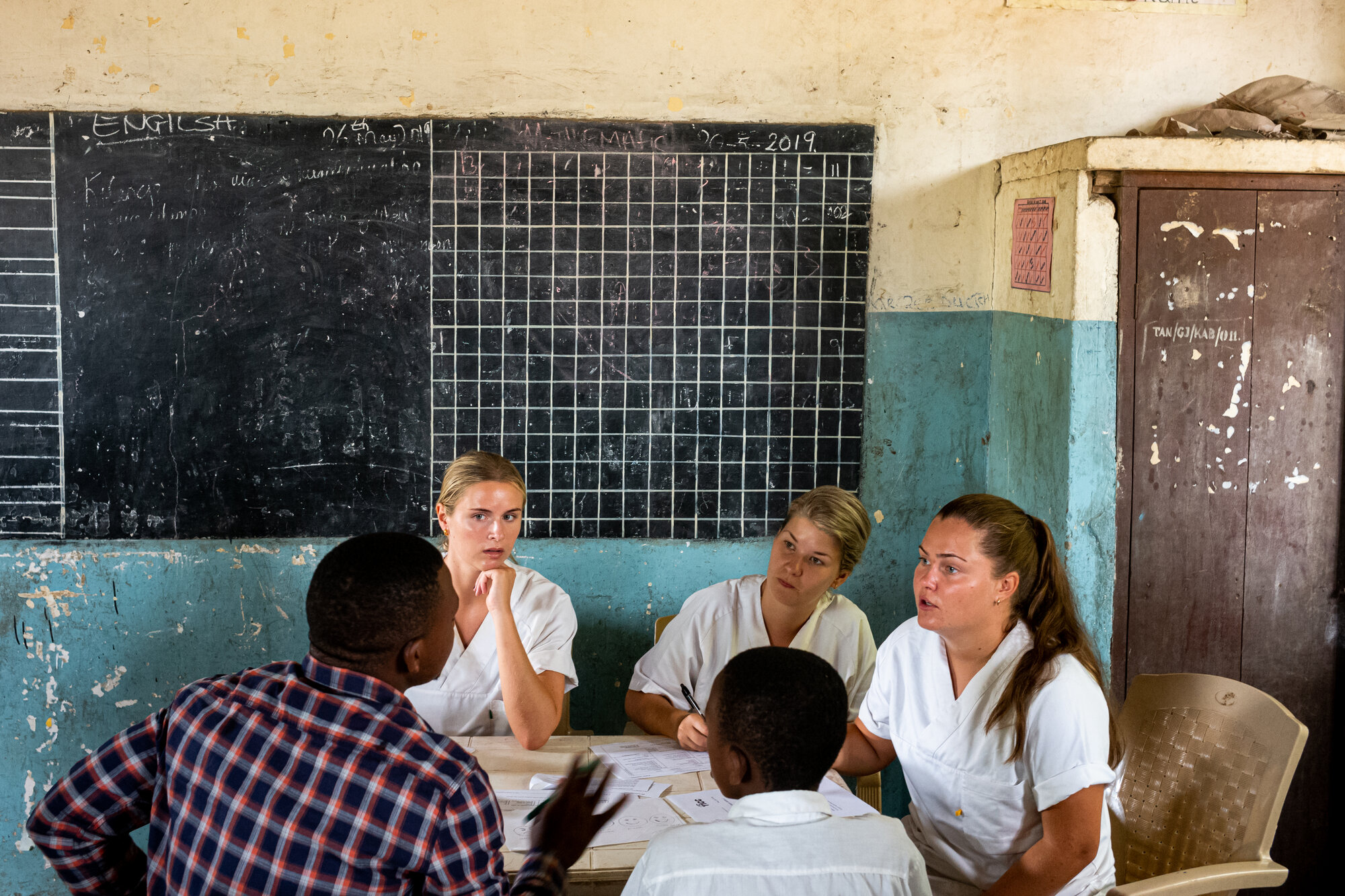 Bildet viser tre sykepleierstudenter fra Norge som er i Tanzania. De sitter og snakker med to afrikanske menn.