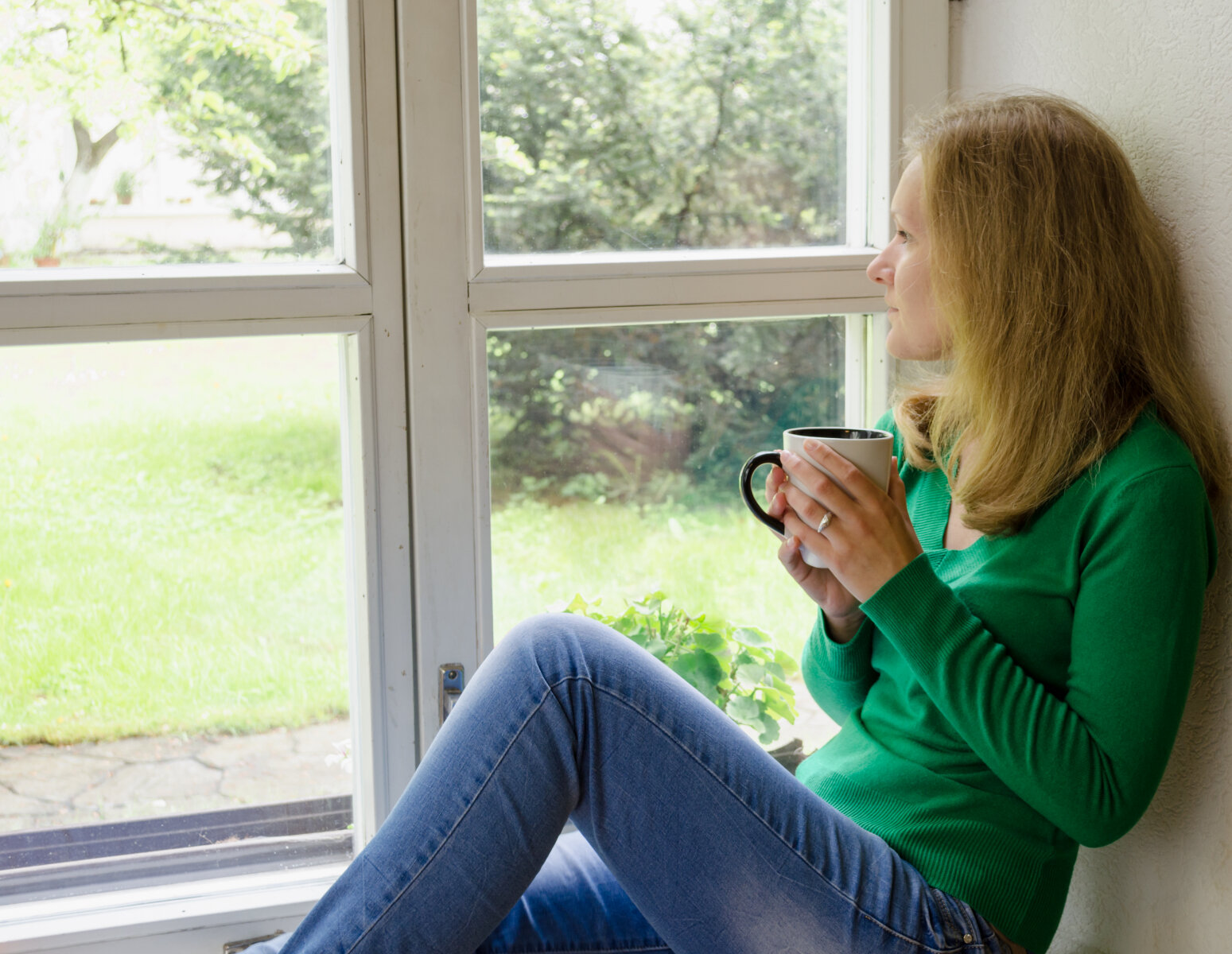 Bildet viser en kvinne som sitter og ser ut av et vindu.