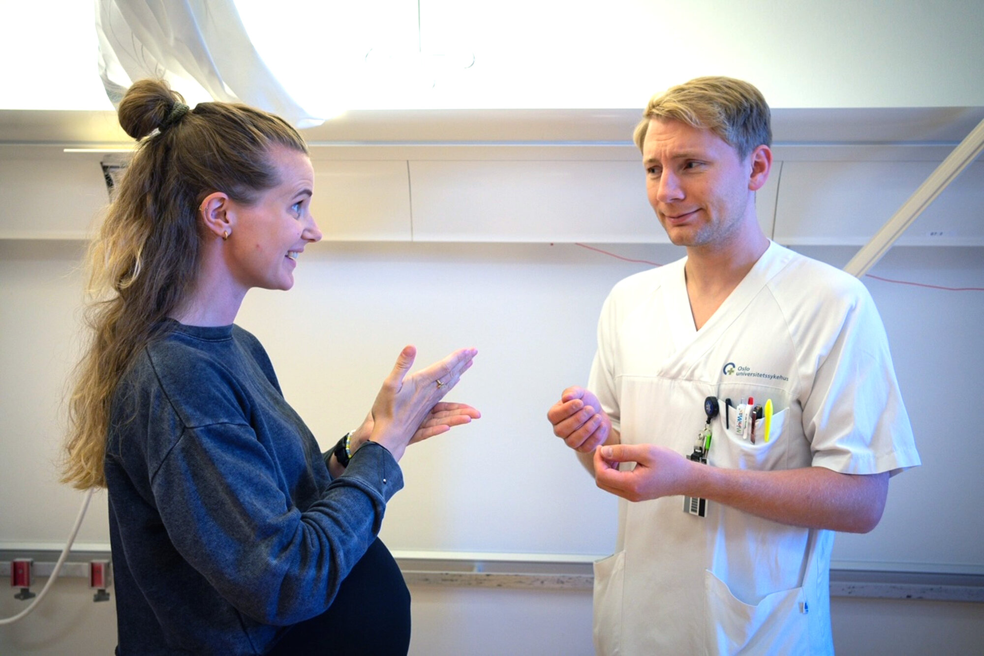 Bildet viser en døv kvinnelig pasient som snakker tegnspråk med en mannlig sykepleier