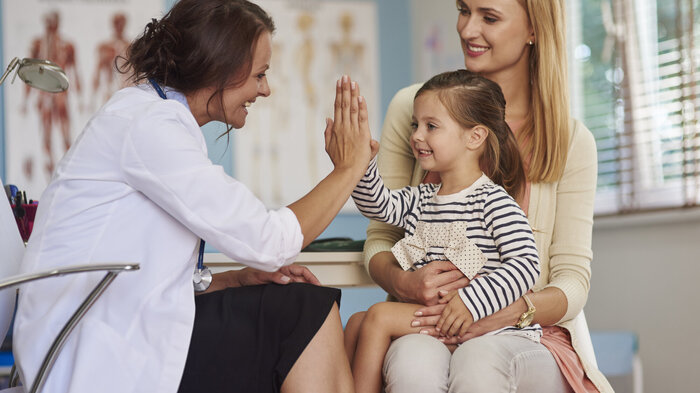 Bildet viser en liten datter på fanget til mora. Dattera gjør high five med en helsesykepleier som sitter overfor dem