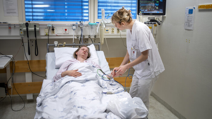Bildet viser en sykepleier som står ved sengen til en pasient på sykehus