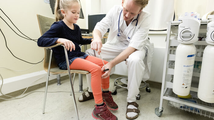 Bildet viser en lege som sjekker refleksen på et barns kne