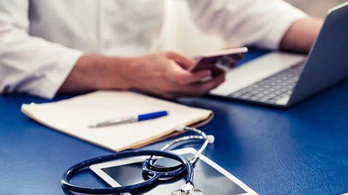 Mobil, pc, stetoskop Bildet viser en hånd som holder i en mobiltelefon.