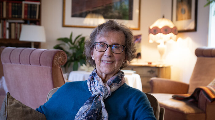 Signy Romslo sitter hjemme i soffa og siler til kamera