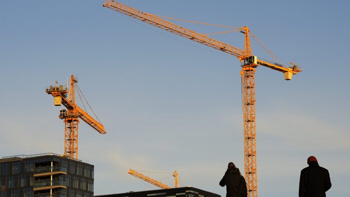 Bildet viser en byggeplass med to mennesker i siluett i forgrunnen