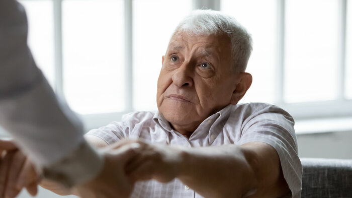 Demensomsorg Bildet viser en eldre mann som holder hendene til noen utenfor bilderammen