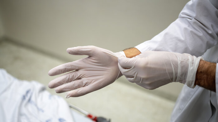 Bildet viser hendene til en lege som tar på hansker.