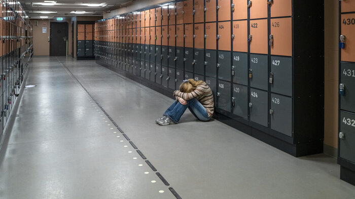 Bildet viser en ungdom som sitter i en korridor