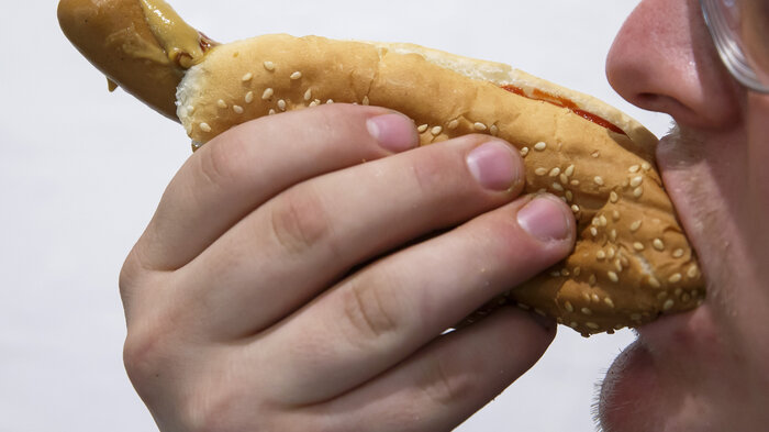 Bildet viser en mann som spiser en pølse i brød.