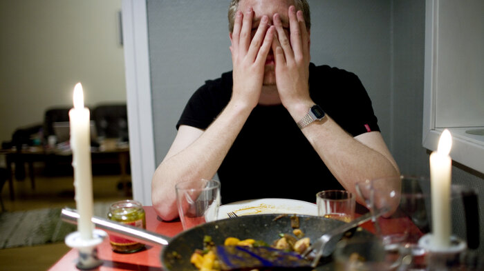 Bildet viser en mann som sitter ved et spisebord og holder seg til ansiktet.