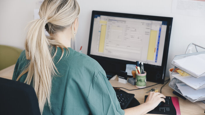 Bildet viser en sykepleier som sitter ved en datamaskin.