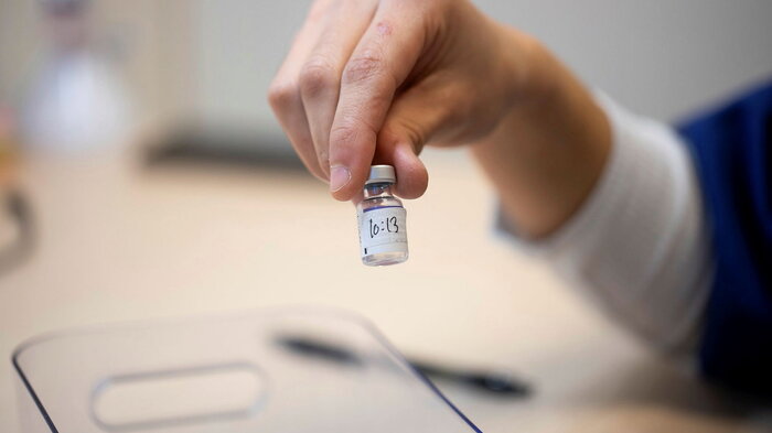 Bildet viser en hånd som holder opp en flaske med koronavaksine