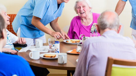 Bildet viser en smilende sykepleier sammen med fornøyde beboere ved et sykehjem.