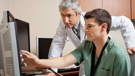 Bildet viser en sykepleier og en lege som kikker på noe på en dataskjerm. Sykepleieren peker på skjermen