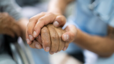 Bildet viser en sykepleier som holder en eldre pasient i hånden.