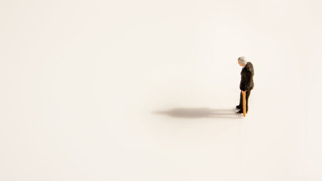 Bildet viser en figur av en gammel mann med stokk som står helt alene.