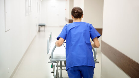 Travel sykepleier med seng i sykehuskorridor