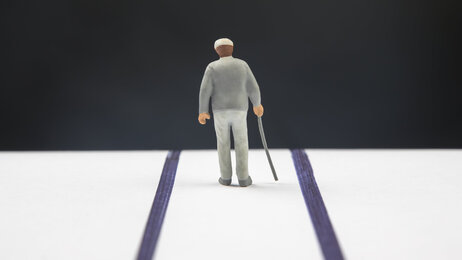Bildet viser en figur av en gammel mann med stokk bakfra