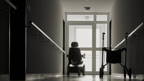 Bildet viser en sykehjemsbeboer i rullestol som sitter ved vinduet i enden av en korridor