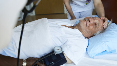 Bildet viser en sengeliggende mannlig pasient som får pleie av to sykepleiere
