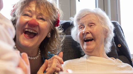 Bildet viser en klokkeklovn på et sykehjem sammen med en eldre kvinne. Kvinnen ler.