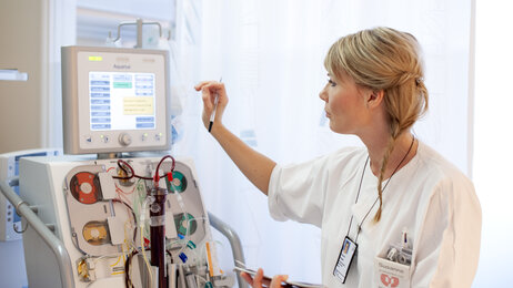 Bildet viser en intensivsykepleier som trykker på en skjerm på en maskin med masse slanger og annet utstyr