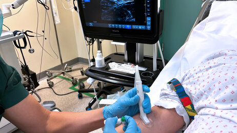 The photo shows a nurse using ultrasound to locate a vein before catheterisation