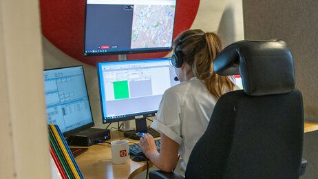 The photo shows a telephone operator sitting at the emergency medical communication centre in front of many computer screens