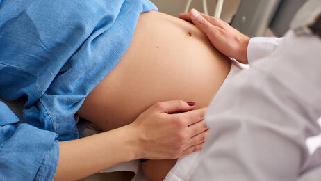Bildet viser en gravid dames mage. Hendene til en lege eller sykepleier undersøker magen