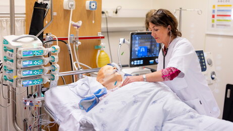 Bildet viser en simuleringsdukke på respirator. En sykepleier står lent over senga.