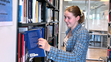 Bildet viser innleggsforfatteren som tar en bok ut av en bokhylle