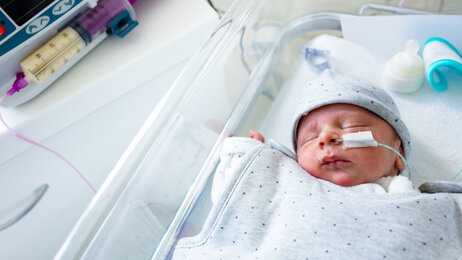 Bildet viser en baby i en sykehusseng. Den har sonde i nesten, og en spr&oslash;yte med morsmelk ligger ved siden av