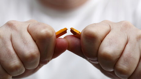 Nærbilde av at en mann knekker en blyant i to.