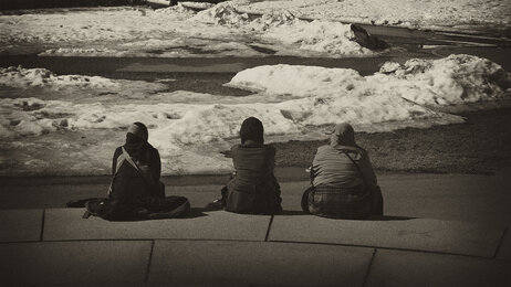 Bildet i sort og hvitt viser tre innvadrerkvinner bakfra som sitter på en steintrapp. Det er avstand mellom dem og de ser utover landskapet.