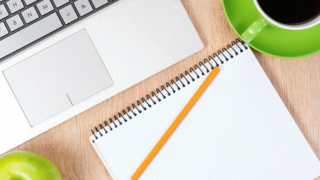 Bildet viser deler av en bærbar PC, en skriveblokk, et eple og en kaffekopp.