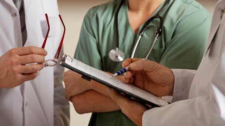 Leger og sykepleiere står og sjekker en journal til en pasient.