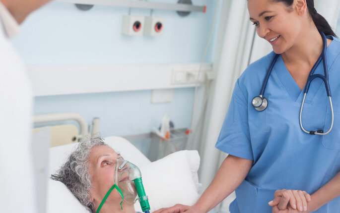 Bildet viser en pasient i sengen med maske, mens en sykepleier står ved siden av