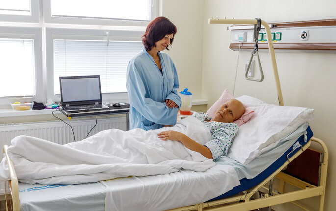 Bildet viser en kvinne som står ved sengen til en døende kvinnelig kreftpasient