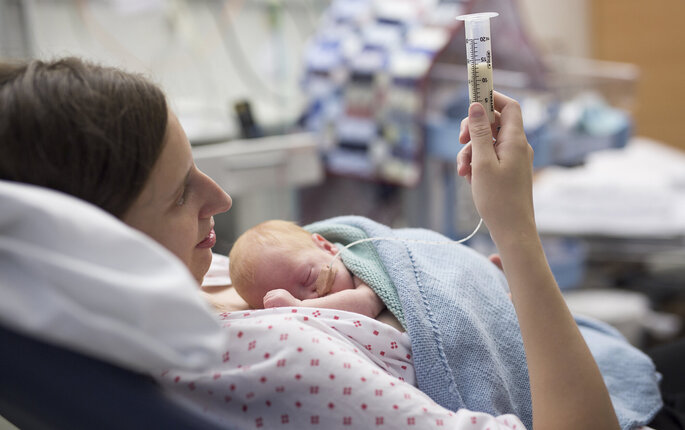 Bildet viser en kvinne på nyfødtintensiven. Hun ligger i sengen og mater sin nyfødte baby ved hjelp av sonde