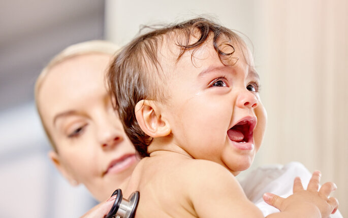 Bildet viser et lite barn som gråter mens en sykepleier lytter på ryggen til barnet