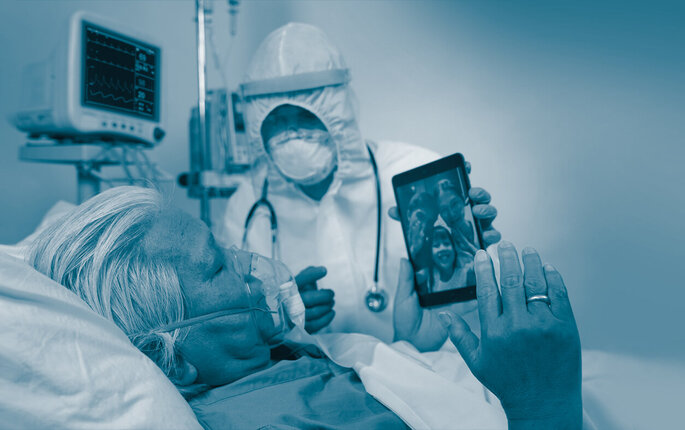 The image shows an intensive care patient with a mask communicating with his family on an iPad.