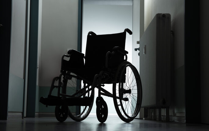 Bilde viser en tom rullestol på et pasientrom i motlys