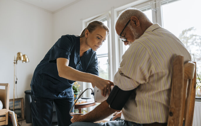 Bildet viser en sykepleier som måler blodtrykket på en eldre pasient i hjemmet