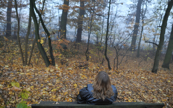 Bilde viser en dame som sitter på en benk med ryggen til